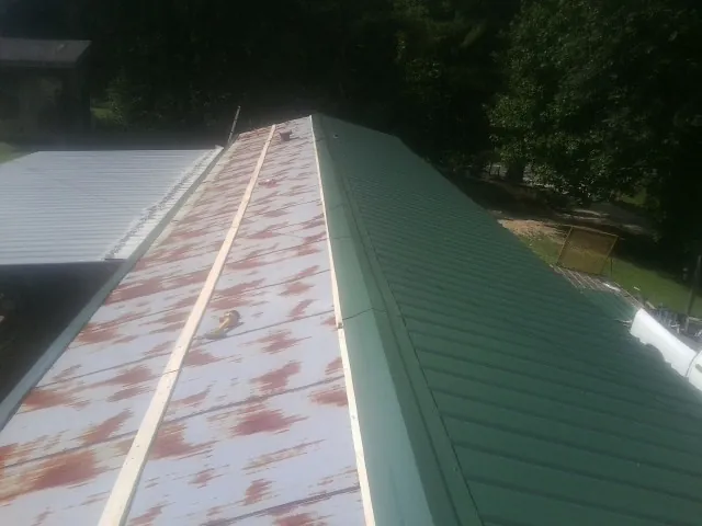 Old rusted panels beside newly installed green metal roofing — Wind Damage Roof Repair by Roofing Brothers in Roberts