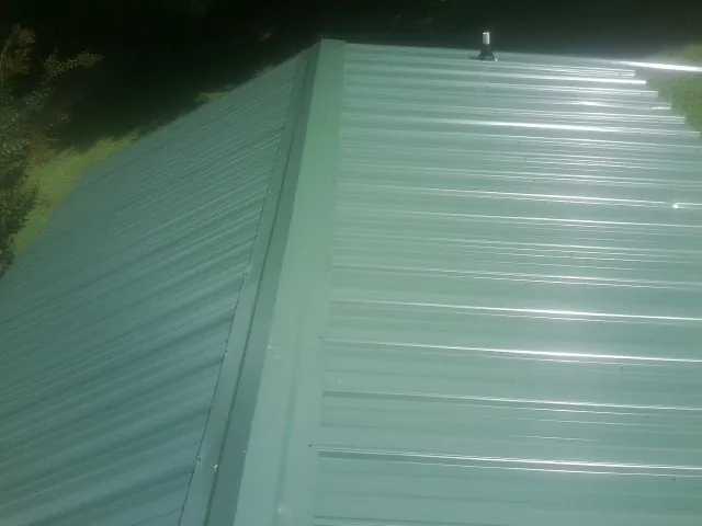 New green metal panels meeting at the ridge of a roof — Flat Roof Repair work by our crew in Roberts