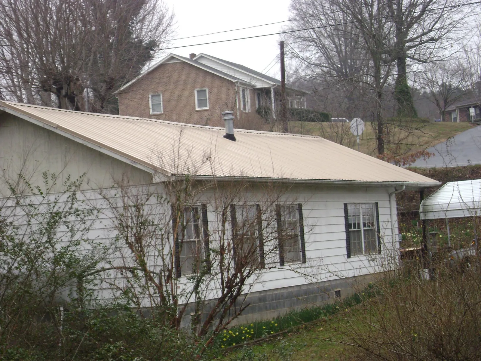 Tan metal roof on a white sided house set into a hillside — Commercial Roofing by Roofing Brothers in Roberts